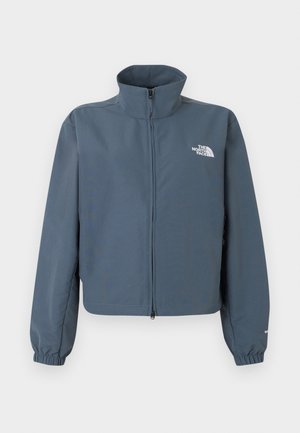 Sininen vetoketjullinen takki, jossa korkea kaulus, joustavat hihansuut ja valkoinen The North Face -logo vasemmalla rinnalla.