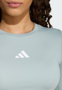 Jasnozielony sportowy top z gładkiej tkaniny z białym logo Adidasa i okrągłym dekoltem, podkreślający dopasowaną sylwetkę.