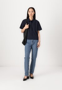 Camisa de manga corta azul marino, jeans rectos de color azul claro y zapatos de tacón negros; sosteniendo un bolso tote negro; diseño minimalista.