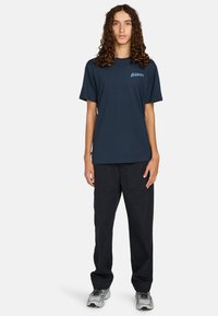 Marineblauwe katoenen T-shirt met een ronde hals en korte mouwen, voorzien van een lichtblauw "ELEMENT" logo op de linkerborst. Gecombineerd met zwarte broek.