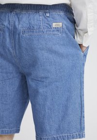 Pantalones cortos de mezclilla con cintura elástica, bolsillos, tono azul y una textura sutil con una etiqueta en la parte posterior.