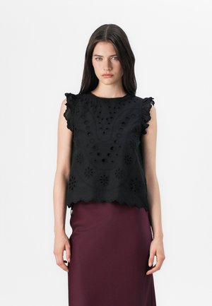 Modell iført en svart brodert topp med volanger og et maroon skjørt, står mot en hvit bakgrunn.