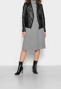 Veste de moto en cuir noir sur une robe grise côtelée, associée à des bottines noires brillantes avec un talon bloc et une fermeture éclair dorée.