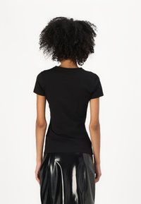 T-shirt nera aderente a maniche corte, con scollatura a girocollo e texture liscia, abbinata a una gonna a tubino nera lucida.