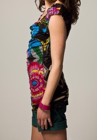 Camicia a maniche corte con stampa floreale e animale vivace, caratterizzata da un design blu e rosa su sfondo nero; abbinata a pantaloni corti scuri e un braccialetto rosa.