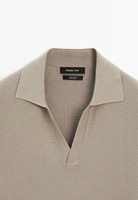 Beige pletená polo košile z 100 % bavlny, s krátkými rukávy, V-výstřihem a jemným texturovaným vzorem na látce.