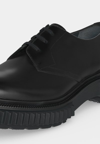Chaussure en cuir noir à lacets avec une semelle épaisse et robuste et des coutures détaillées le long des bords supérieurs.