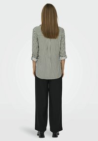 Gestreept overhemd in groen en wit, met opgerolde mouwen, gecombineerd met losse zwarte broek en zwarte schoeisel, gezien van achteren.