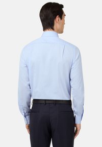 Camicia azzurra chiara con maniche lunghe, polsini a bottone e colletto classico, indossata con pantaloni scuri su misura e una cintura nera.