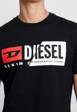 T-shirt noir avec une couture diagonale et un logo Diesel audacieux en blanc et rouge, texte "Denim for successful living" visible sur la poitrine.