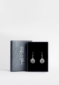 Silvriga örhängen med blommönster, visade i en mörk, sammetsklädd ask med en strukturerad silverfärgad yta och präglad logga på locket.