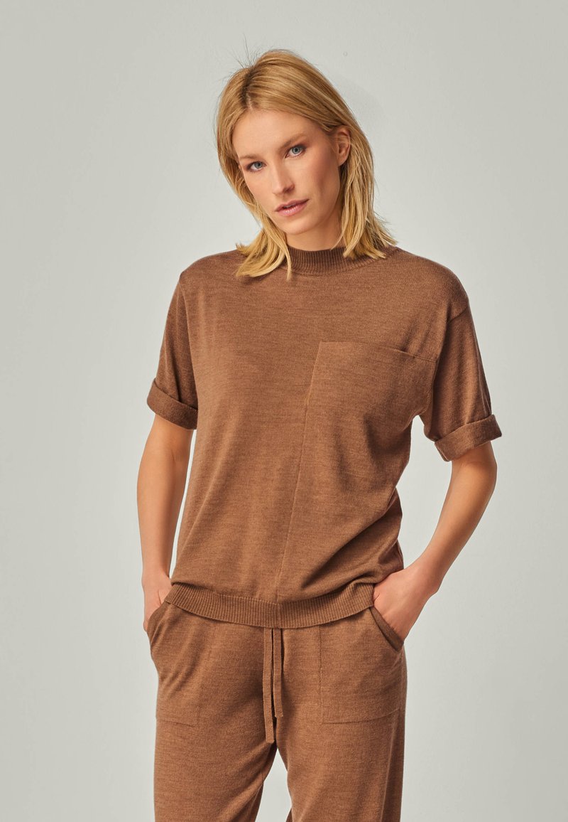 Brown knitted sweater with short rolled sleeves, featuring a front pocket and a ribbed neckline. Paired with matching brown joggers.