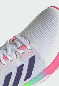 Weißer Sportschuh mit strukturiertem Obermaterial, rosa Schnürsenkeln und lila Drei-Streifen-Logo. Die Sohle hat ein Farbverlauf-Design.