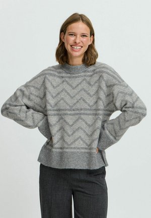 Pull en tricot gris avec un motif en zigzag, des manches larges et un ourlet côtelé, offrant une coupe décontractée et une texture douce.