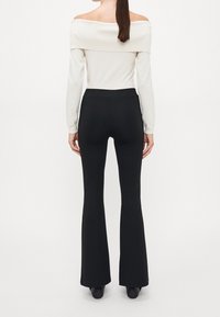 Top blanco de canalé con los hombros al descubierto, combinado con pantalones negros ajustados de campana. La blusa tiene mangas largas y un escote amplio.