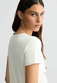 Witte katoen t-shirt met een ronde halslijn en korte mouwen, met een grafisch ontwerp op de voorkant in rode en zwarte accenten.