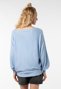 Hellblauer, übergroßer Pullover mit langen, ballonförmigen Ärmeln, weicher Textur und gerippten Bündchen, kombiniert mit dunklen Shorts. Rückansicht angezeigt.