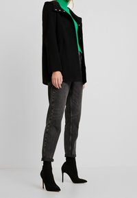 Černý kabát se stříbrnými patentkami, nošený přes zelený rolák. Šedé džíny s ohrnutými nohavicemi, doplněné černými lodičkami na vysokém podpatku.