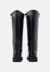 Μαύρες μπότες μέχρι το γόνατο με λείο δέρμα, διαθέτοντας στρογγυλεμένη μύτη και επίπεδο, σταθερό τακούνι. Λεπτομέρειες με θηλιά στο πίσω μέρος για εύκολη εφαρμογή.