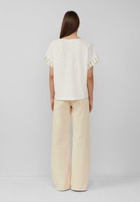 Losse witte top met korte mouwen en gestreepte lichtgroene accenten op de mouwen, gecombineerd met lange crèmekleurige broek. Gladde textuur.