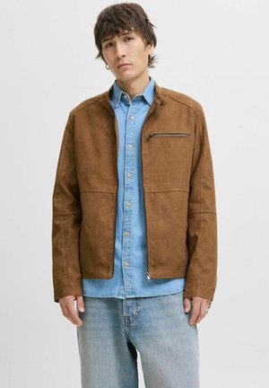 Brun suedeblazer med en lynlåslomme, der har en simpel krave og syede detaljer, lagdelt over en lyseblå denimskjorte.