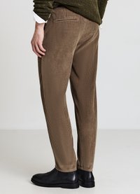 Pantaloni di velluto a coste marroni con design a gamba dritta, caratterizzati da una texture a coste e tasca laterale, abbinati a stivaletti neri alla caviglia.