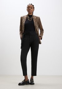 Blazer con stampa leopardata sopra un top nero a coste, abbinato a pantaloni neri a vita alta e mocassini neri in vernice con dettagli in oro.