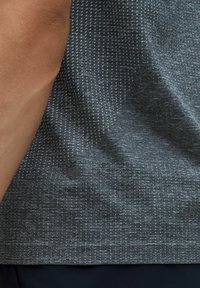 Ciemnoszara koszulka sportowa z teksturowanego materiału, z delikatnym wzorem. Logo w lewym dolnym rogu. Krótkie rękawy, swobodny krój.