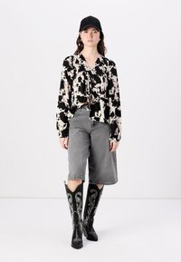 Bluza s uzorkom u crno-bijeloj boji s vezicom sprijeda, sive kratke hlače s visokim strukom i crne čizme do koljena s bijelim vezom. Crna kapica.