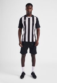 Sorte og hvide stribede trøje med korte ærmer, parret med sorte shorts. Har et lille logo på brystet og sorte sportssko.
