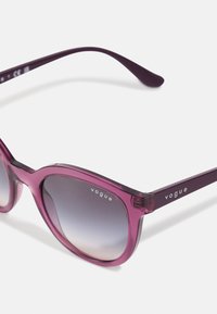 Ochelari de soare transparenți violet, cu o formă supradimensionată de ochi de pisică. Lenti în degrade și logo-ul "vogue" pe brățări. Finisaj neted și design elegant.