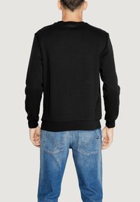 Sudadera negra de cuello redondo con mangas largas, textura suave y puños acanalados, combinada con jeans de mezclilla azul claros que tienen bolsillos traseros.