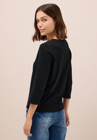 Haut long en coton noir avec un col rond, texture lisse et coupe décontractée, associé à un jean en denim bleu délavé.