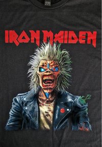 Černé grafické tričko s potiskem postavy monstra s trnitými blond vlasy, modrýma očima, která nosí roztrženou koženou bundu. Text "IRON MAIDEN" nahoře.