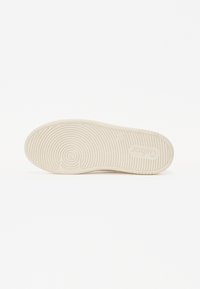 Kengän pohja off-white kumista, jossa on pyöreä ja lineaarinen kuvio, mukana logo ja sileä pinta.