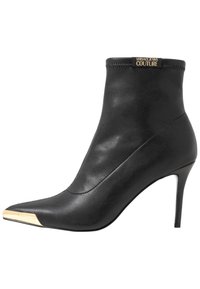 Czarne botki za kostkę z gładkiej skóry, ostro zakończony nosek, wysoki obcas na szpilce oraz złoty akcent na nosku. Logo Versace Jeans Couture.