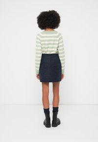 Suéter a rayas verdes y blancas con mangas largas, combinado con una falda azul oscuro texturizada y botines negros con suelas gruesas.