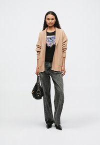Beige oversized knitted cardigan, black graphic t-shirt with blue and pink design, gray high-waisted jeans, black handbag, pointed black shoes.
