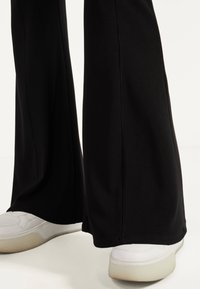 Svarta ribbade byxor med en utsvängd silhuett, som har en slät tygtextur. Kombineras med vita sneakers med gummisula.