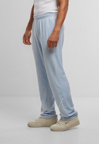 Pantaloni felpa azzurri chiari con vita regolabile, tasche laterali e dettagli di cucitura sottili. Tessuto dalla texture liscia. Frontale piatto e gambe affusolate.