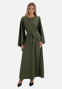 Robe maxi vert olive en tissu lisse, dotée de longues manches et d'une taille cintrée avec un détail de lacets décoratifs.