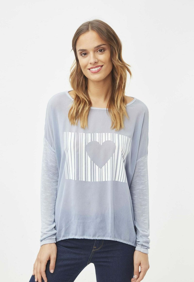 Camiseta de manga larga de color azul claro con un gráfico blanco que presenta líneas verticales y un diseño de corazón en el centro. Tela suave y texturizada.