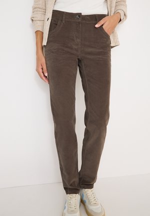 Brune fløjl bukser med slim fit, der har sidelommer og lukning med knap foran. Kombineret med lyse sneakers.