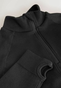 Schwarzer Pullover mit hohem Kragen, der eine gerippte Textur und einen halben Reißverschluss aufweist. Die Ärmel zeigen ein enganliegendes Design mit gerippten Bündchen.