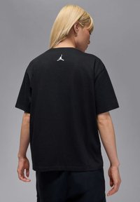 Must 黑色棉neeluga, lühikeste varrukate ja ümmarguse kaelusega, millel on väike valge Jumpman logo ülemisel seljal.