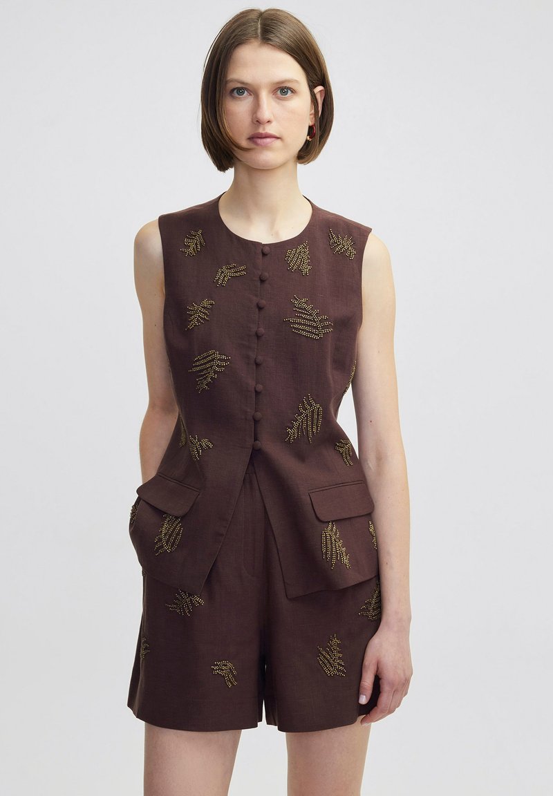 Bruin linnen mouwloze playsuit met gouden kraalborduursel, knopen aan de voorkant en patchzakken op de taille. Op maat gemaakt pasvorm met korte pijpen.