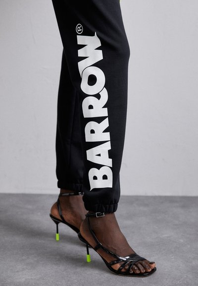 Black joggers with large white "BARROW" text, elastic cuffs, paired with shiny black strappy heels featuring neon green accents.