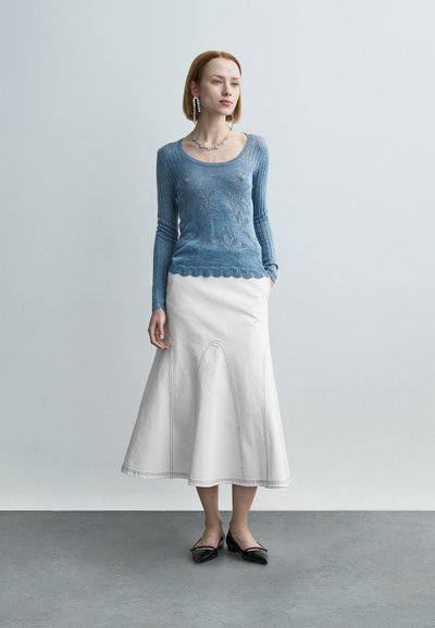 Pull en tricot côtelé bleu clair avec motif floral, assorti à une jupe blanche évasée longueur genou avec ourlet festonné et coutures. Ballerines noires.