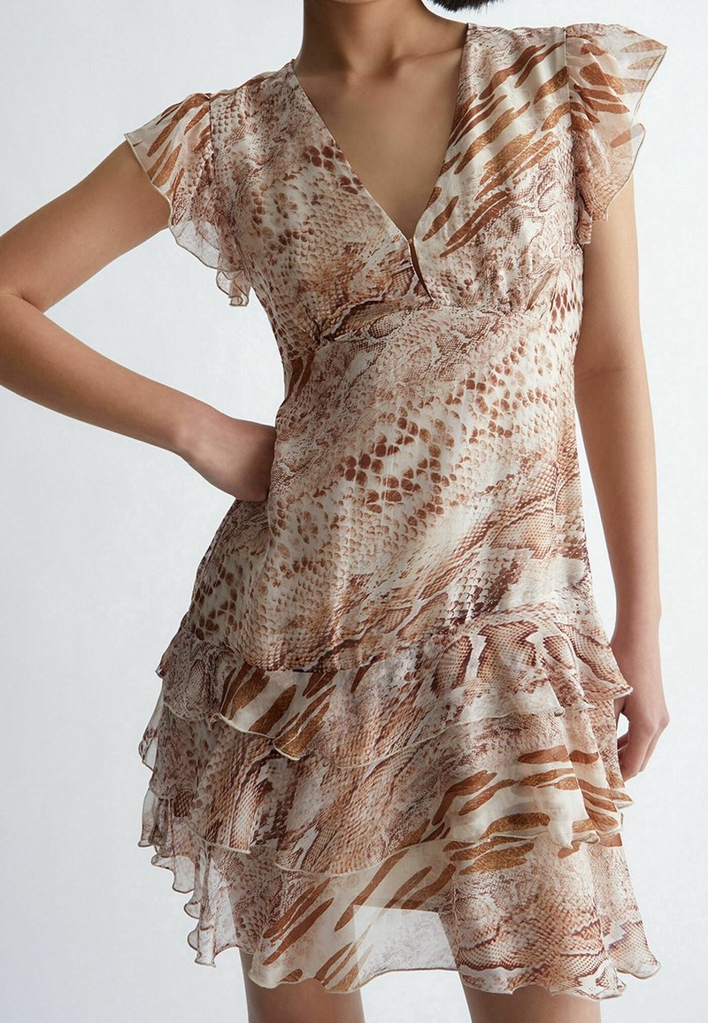 Femme portant une robe courte à volants avec des manches froncées et un motif serpent marron et beige.