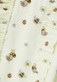Tissu à motifs avec un fond jaune clair et des illustrations d'abeilles, de coccinelles et de fleurs ; détail de bord en volants.